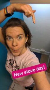 selfie of a person pointing dramatically at the empty space in her kitchen with the text 'New stove day!'