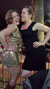 two girls posing for the camera, one wearing black and the other wearing sparkling gold, and sticking their tongues out