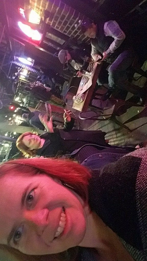 a sideways selfie of a person smiling and a view of a bar porch lit with harsh neon behind her