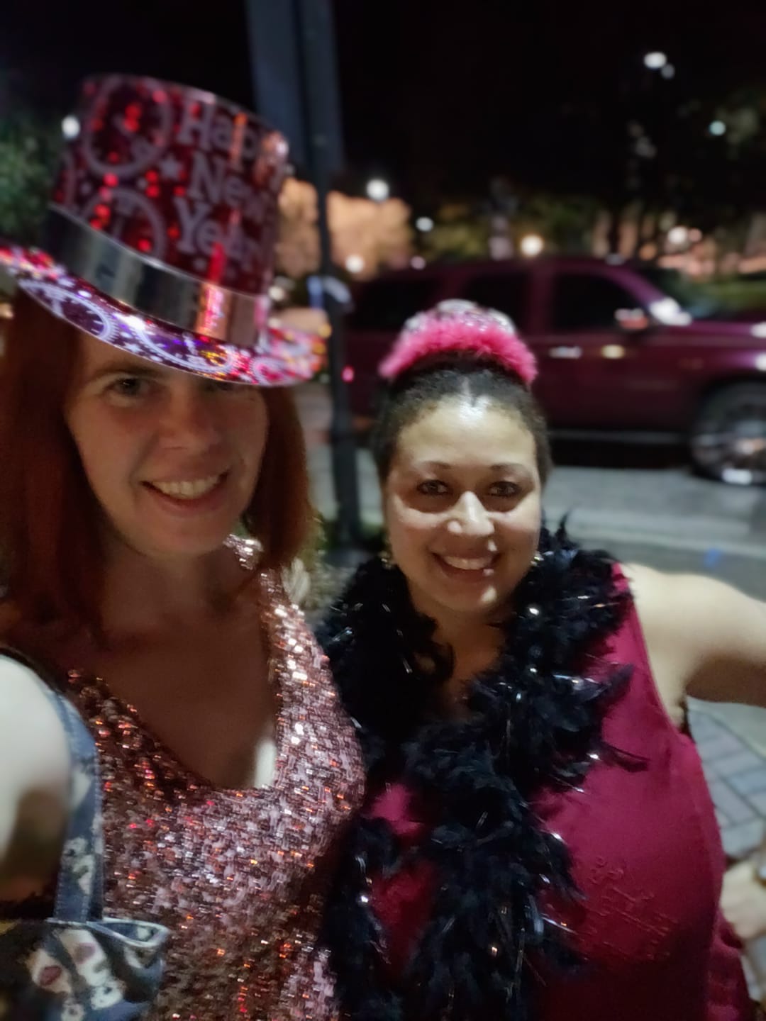 a selfie of two people in glittery clothing with a night city view behind them