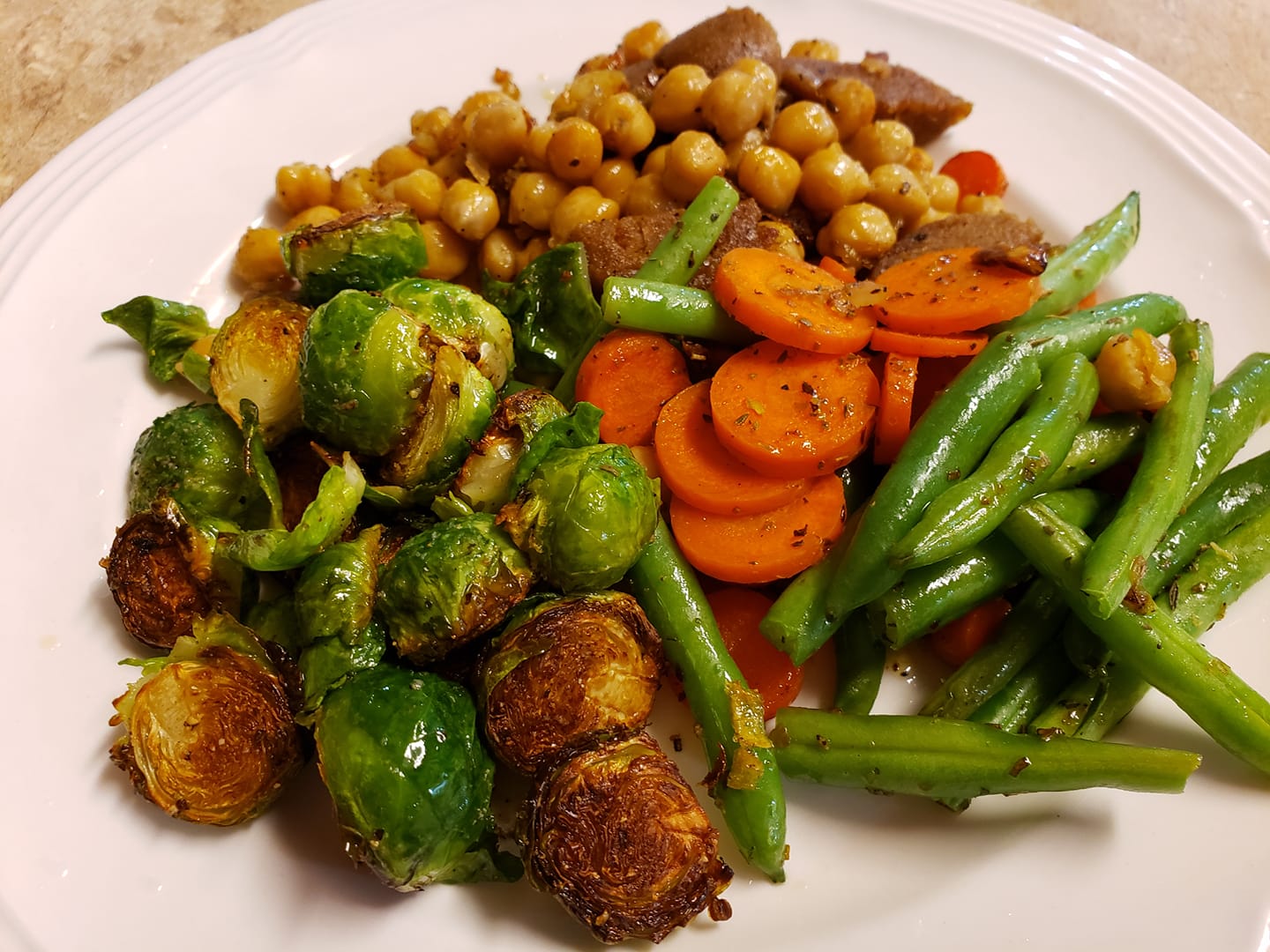a dinner plate with roasted vegetables like carrots and brussels sprouts and some kind of beans