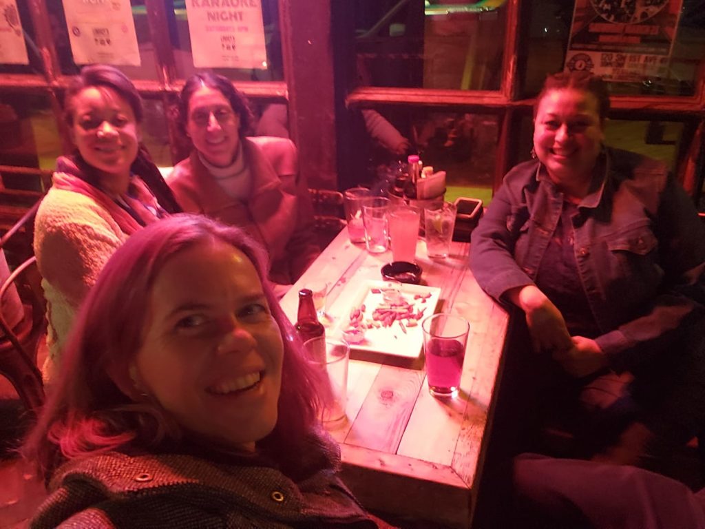 a selfie of a group of people at a bar table under harsh red lighting