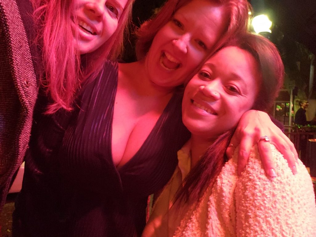 three women smile for a selfie under strong red lighting