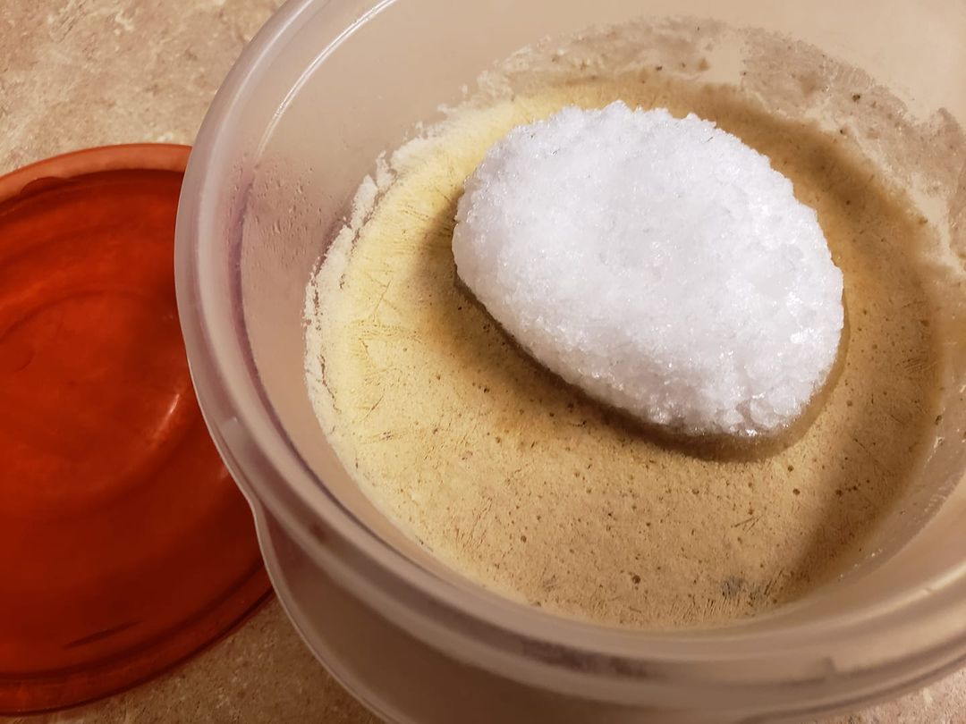 a plastic container with some unknown frozen substance and a small iceberg of freezer frost on top