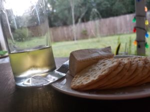 a dramatic shot of a plate of cheese and crackers and a drink with a yard in the blurry distance