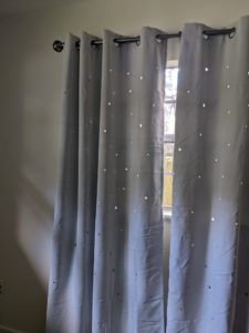 grey curtains against a grey wall but there are small star shaped holes in the fabric letting light through