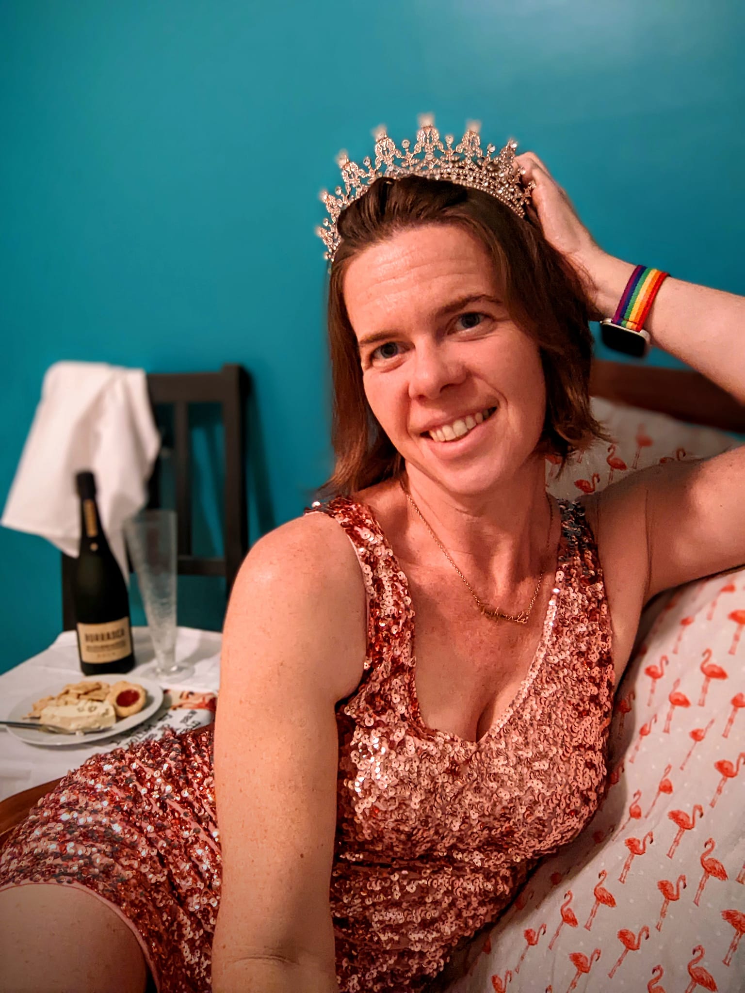 selfie of a person in a tiara and a glittery dress lounging on a chair with a bottle of bubbly and snacks behind her