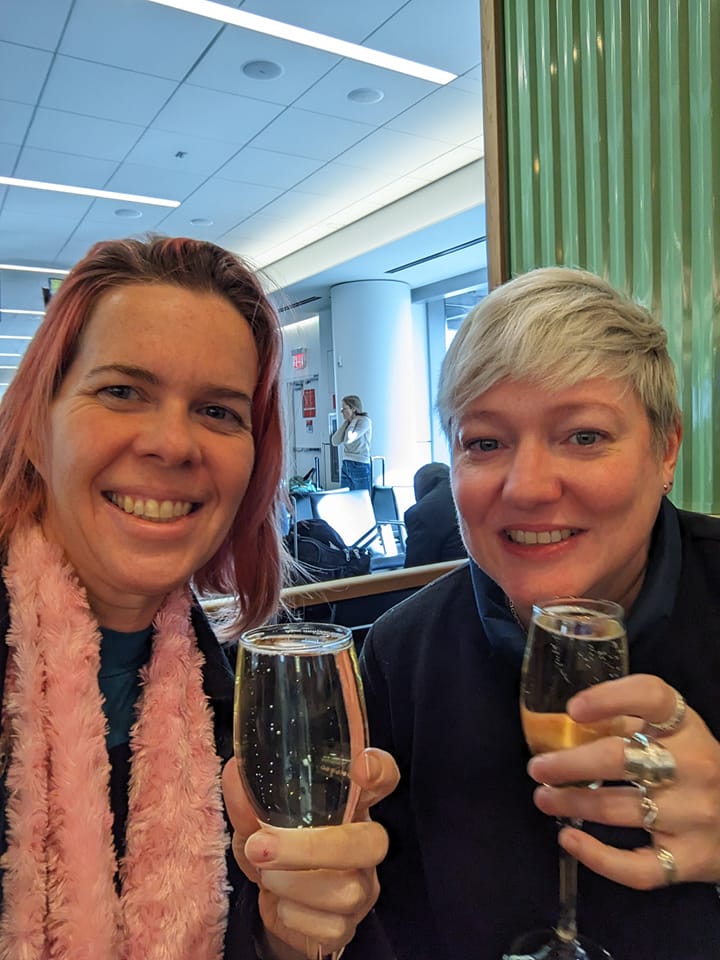 selfie of two women in an airport bar holding up champagne glasses