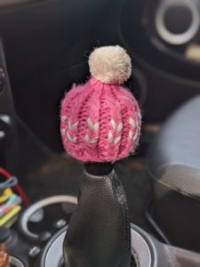 a manual car gear shift with a knitted pink hat with a white bobble on top