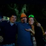 three people on a bar patio lean on a railing and post for a picture