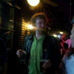 a dark night on a bar patio where a person is holding a drink in each hand