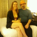 two people dressed for a party are sitting on a bed in a bright hotel room