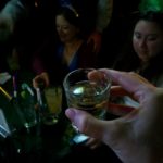 a hand holding a shot glass of fluid against a dark bar scene