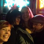 four people pose for a group selfie under colorful bar lights at night