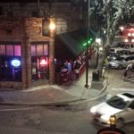 evening view of a city street corner and a bar with colorful lights in its windows