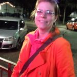a person in a vibrant orange coat and a new years tiara smiles for a picture