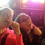 two people are singing under the colorful lights of a bar window