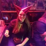 a person with two cone shaped new years hats on smiles at the camera under colorful lights