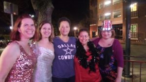 a group of five women in a variety of party clothing pose together on an evening city corner