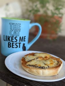 a bagel with melted cheese next to a coffee cup