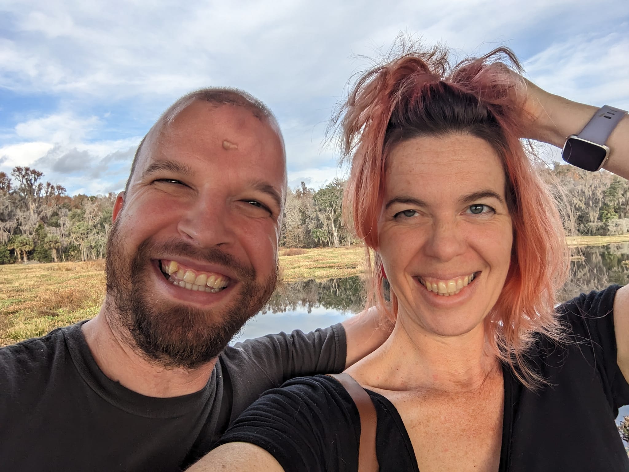 two people pose for a selfie against a nature scene while one rumples the other's hair