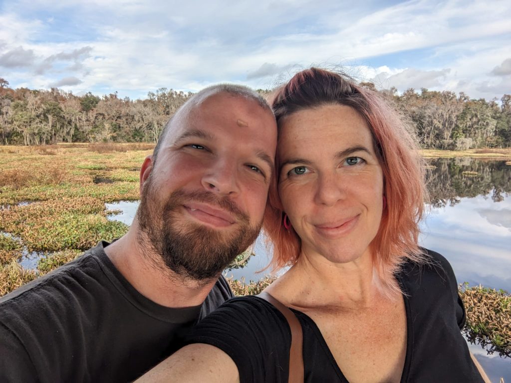 two people taking a selfie with a lake and forest behind them