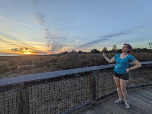 a person is on a wooden boardwalk taking a selfie against a dramatic sunset over a dry prairie