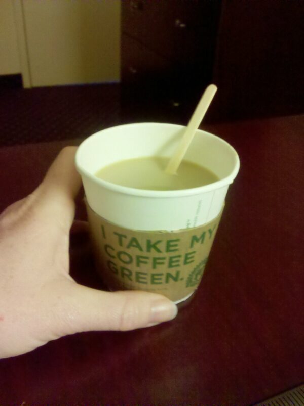 a short cup of htel coffee being held by a hand on a dark cherry wood surface