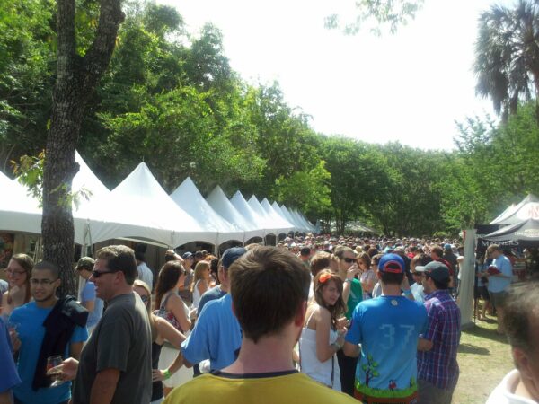 a crowd of people in a park between two rows of white event tents