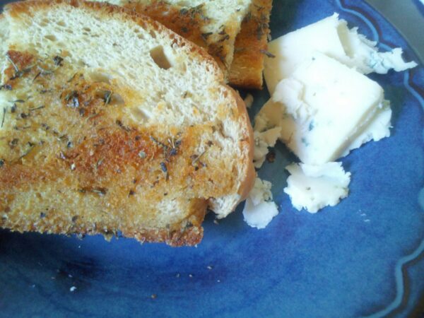 a sandwich is sitting next to a large chunk of veiny blue cheese on a blue plate