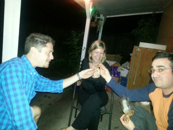 three people on a porch at night raise small object to meet in the middle between them