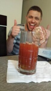 a person in the background makes a thumbs up gesture at a bloody mary drink in the foreground