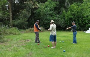 three guys are on a lawn holding small balls and pointing at more balls on the ground