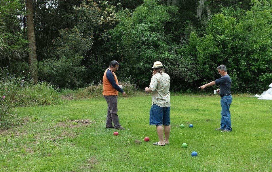 three guys are on a lawn holding small balls and pointing at more balls on the ground