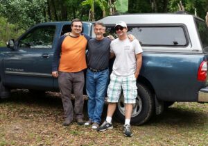 three guys are posing against a dark green truck