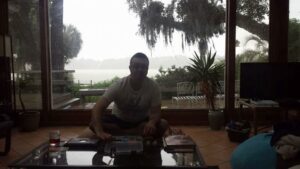 a person sits in shadows in front of a huge window with a cloudy sky and trees