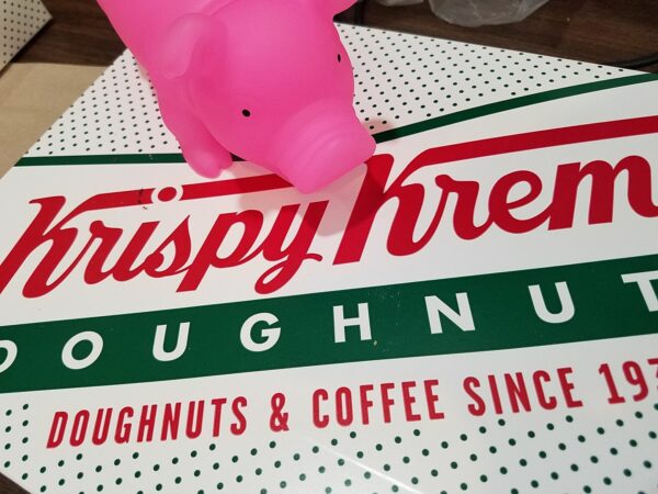 a large plastic pig sits on top of a box of Krispy Kreme donuts
