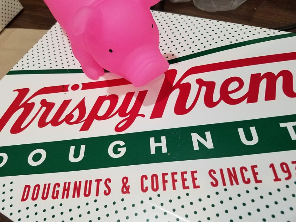 a large plastic pig sits on top of a box of Krispy Kreme donuts
