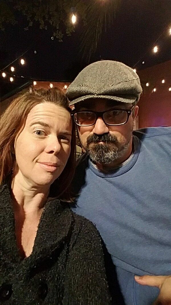 selfie of a couple wearing sweaters on a dark patio with string lights above