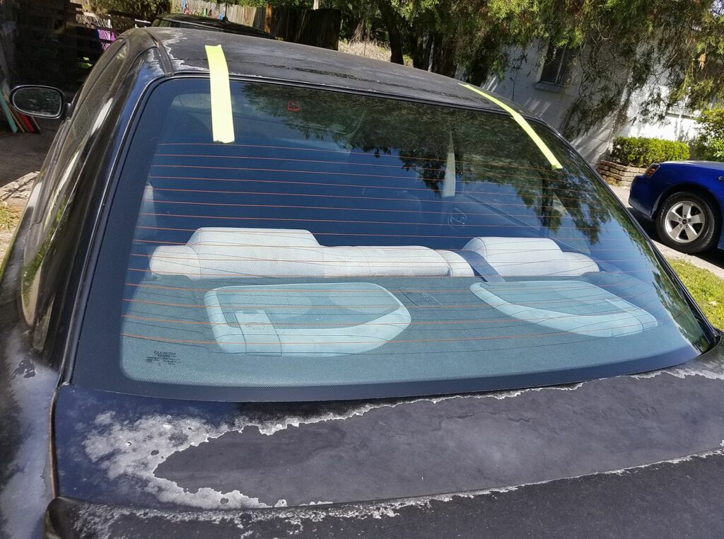 a shiny new glass rear window is freshly set into an old black car with the paint peeling off