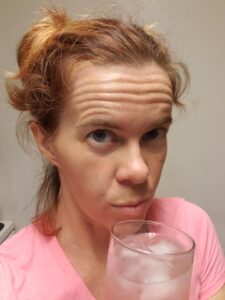selfie of a woman in a pink shirt holding a glass with ice in it