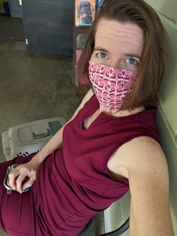 a selfie of a lady wearing a mask that matches her red dress sitting next to a cat carrier