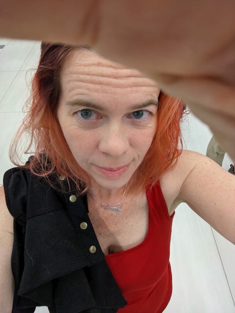 a selfie taken from above with a blurry hand and wearing a red dress with a sweater draped over my shoulder