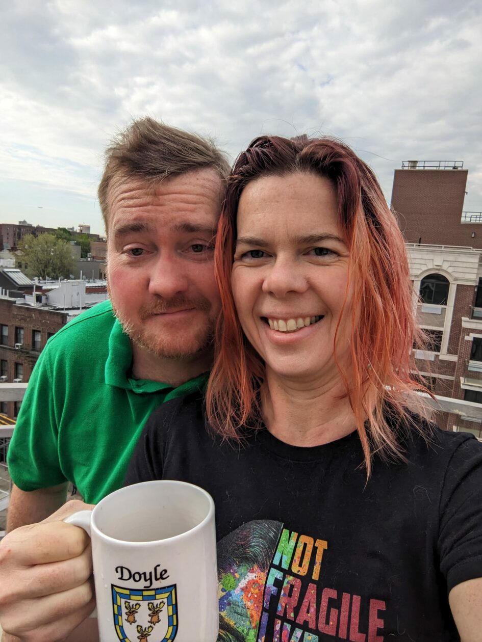 selfie of two people on a rooftop with a city neighborhood behind them