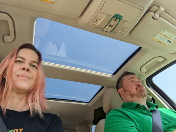 selfie of two people in a car and blue sky through the sun roof above