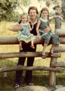 an adult hold on to two children who are sitting on top of a fence made from irregular tree trunks