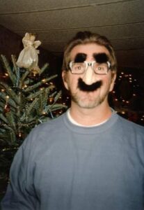 a person in front of a christmas tree is wearing novelty glasses with fake nose and eyebrows and mustace