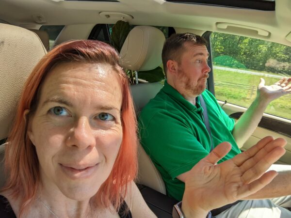 selfie of two people in a car with hands raised in fake confusion