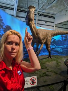 selfie pointing up at a huge dinosaur model