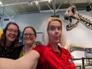selfie with three people and a dinosaur skeleton peeking into the frame